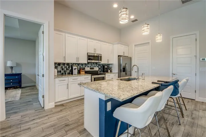 Kitchen featuring appliances with stainless steel finishes, a kitchen bar, a center island with sink, white cabinets, and tasteful backsplash