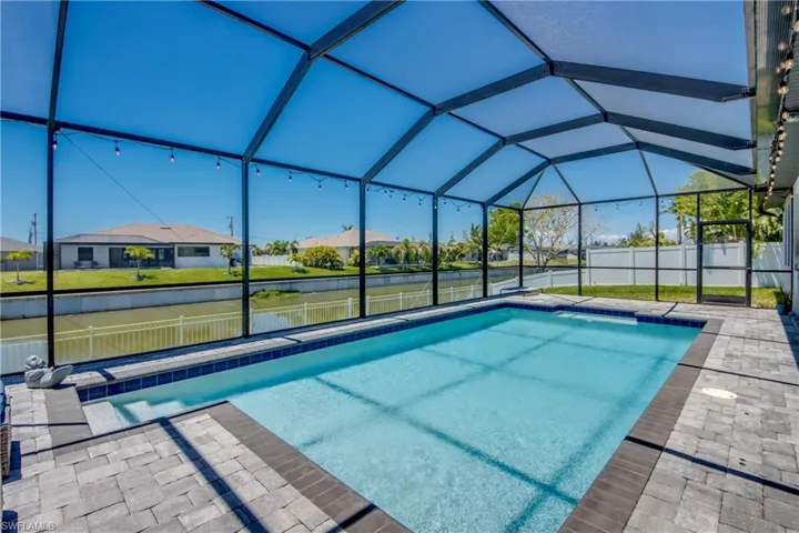 View of pool featuring a water view, fence, glass enclosure, and a residential view