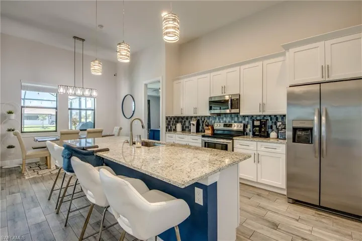 Kitchen featuring appliances with stainless steel finishes, a sink, white cabinetry, backsplash, and light stone counters