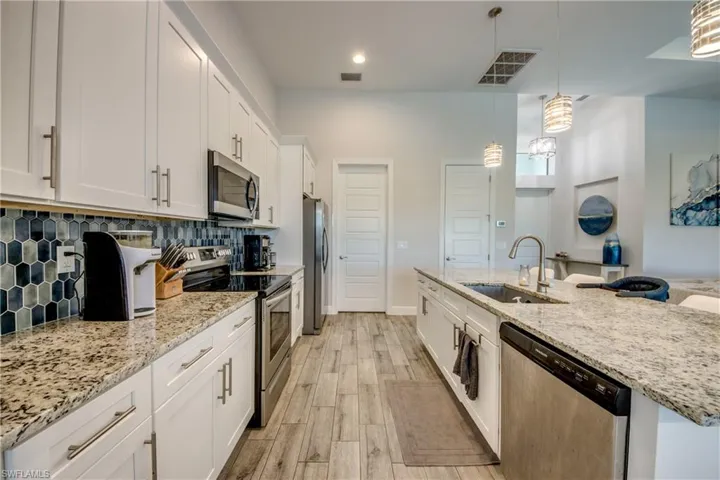 Kitchen with appliances with stainless steel finishes, a sink, white cabinetry, backsplash, and an island with sink