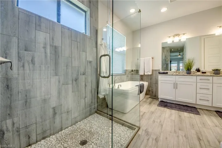 Bathroom featuring tiled shower, a freestanding bath, vanity, tile walls, and wainscoting