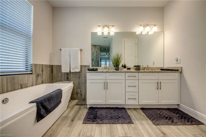 Full bath featuring double vanity, wood finished floors, a soaking tub, tile walls, and a wainscoted wall