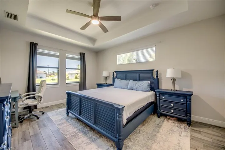 Bedroom featuring a tray ceiling, light wood-style flooring, and baseboards