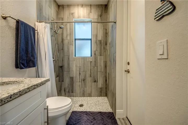Bathroom featuring tiled shower, toilet, vanity, and a textured wall