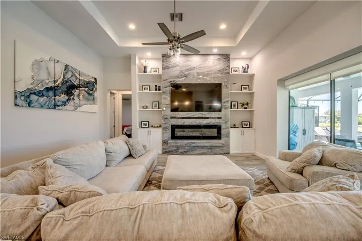 Living room with a tray ceiling, ceiling fan, built in features, a fireplace, and recessed lighting