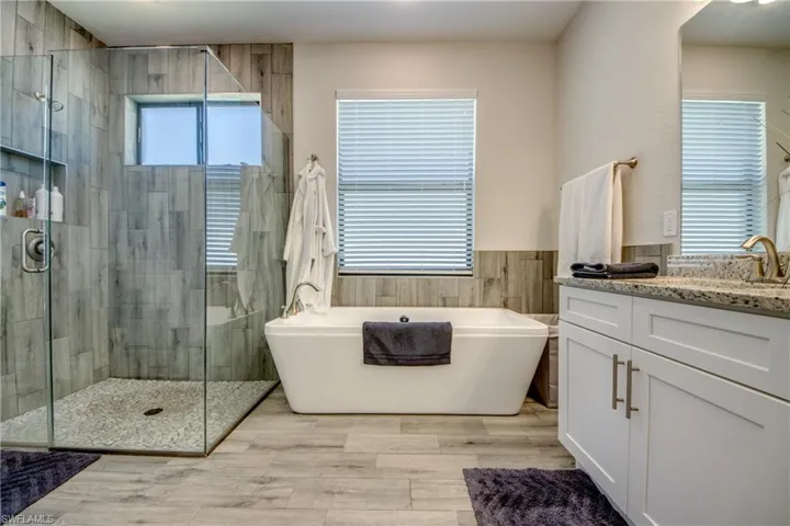 Full bath featuring vanity, a stall shower, a freestanding bath, tile walls, and a wainscoted wall