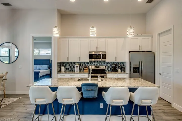 Kitchen featuring stainless steel appliances, a sink, decorative backsplash, white cabinetry, and light wood finished floors