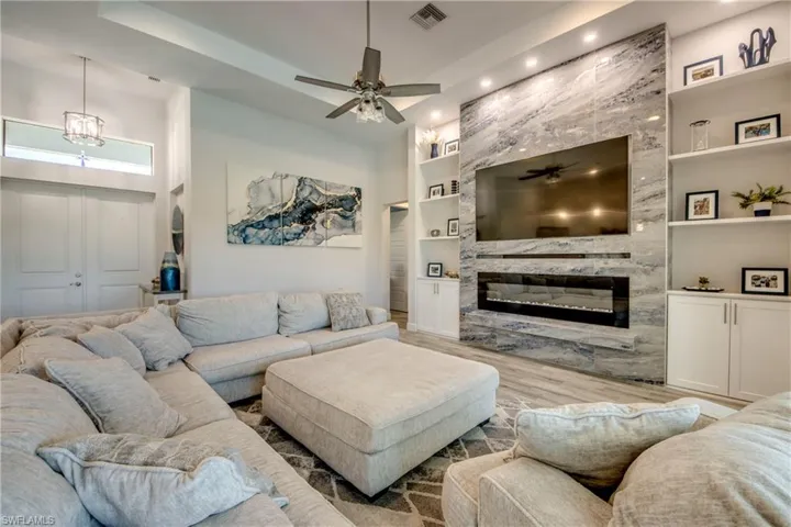 Living area with built in shelves, ceiling fan, a premium fireplace, wood finished floors, and recessed lighting