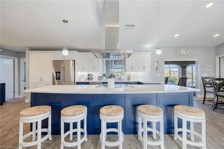 Kitchen with a large island with sink, white cabinetry, light hardwood / wood-style flooring, decorative light fixtures, and high end refrigerator
