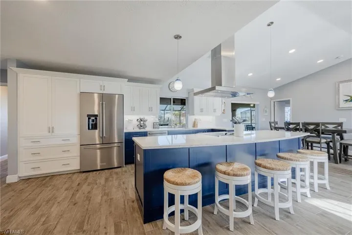 Kitchen featuring pendant lighting, island exhaust hood, high quality fridge, vaulted ceiling, and a center island