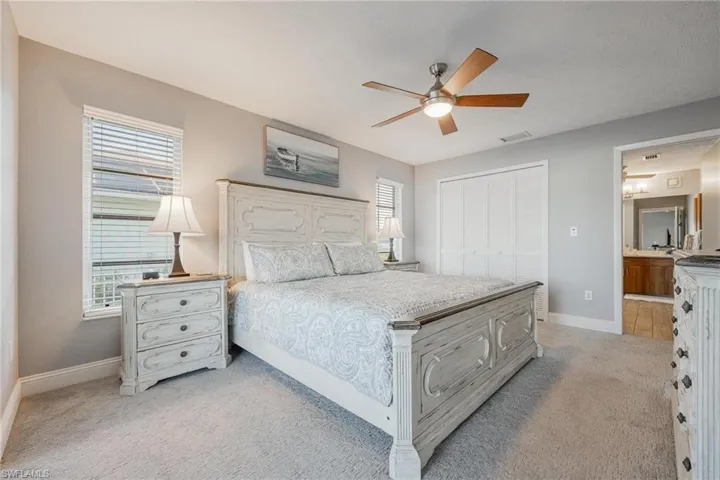 Carpeted bedroom featuring multiple windows, ceiling fan, and a closet