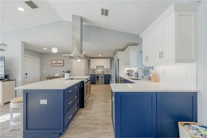 Kitchen with blue cabinets, lofted ceiling, hanging light fixtures, and white cabinetry