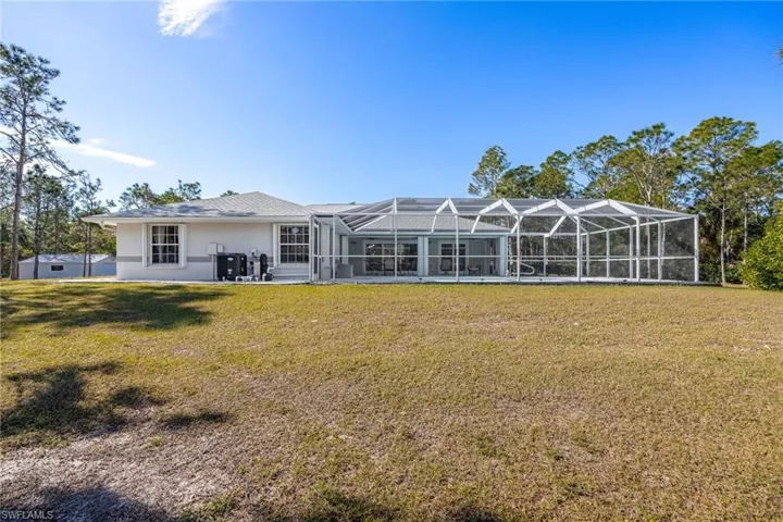 Rear view of property featuring glass enclosure, a lawn, and stucco siding