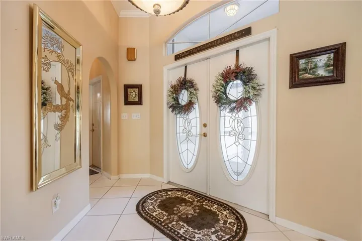 Foyer featuring arched walkways, french doors, crown molding, light tile patterned floors, and baseboards