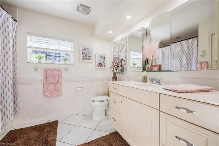 Full bathroom with a wainscoted wall, tile walls, toilet, vanity, and tile patterned floors