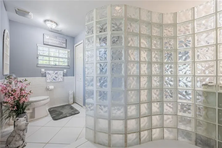 Full bathroom with tile walls, tile patterned floors, toilet, wainscoting, and walk in shower