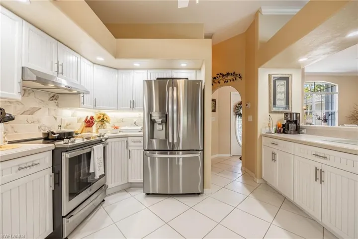 Kitchen featuring arched walkways, decorative backsplash, appliances with stainless steel finishes, light countertops, and under cabinet range hood
