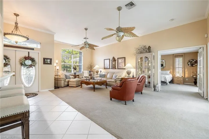 Tiled living room with baseboards, visible vents, ceiling fan, ornamental molding, and carpet flooring