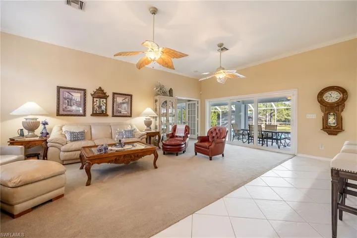 Carpeted living room with tile patterned flooring, a ceiling fan, visible vents, baseboards, and ornamental molding