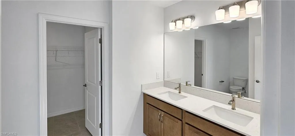 Bathroom with a walk in closet, double vanity, and light tile patterned floors