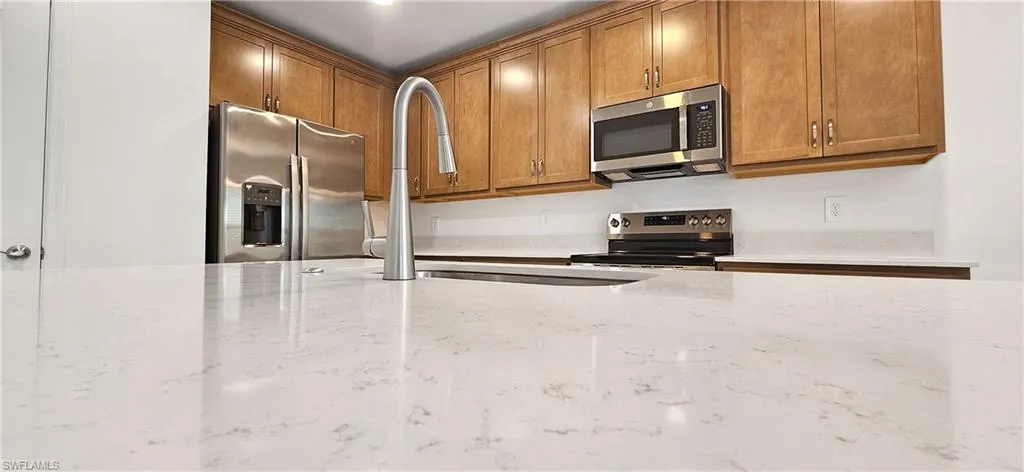 Kitchen with stainless steel appliances, wood finish cabinetry, and light stone counters