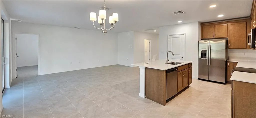 Kitchen featuring wood finish cabinetry, stainless steel appliances, hanging lights, light stone counters, and an island with sink