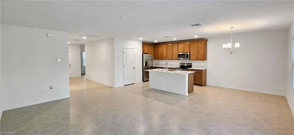 Kitchen featuring stainless steel appliances, wood finish cabinets, hanging lights, a center island with sink, and light stone counters