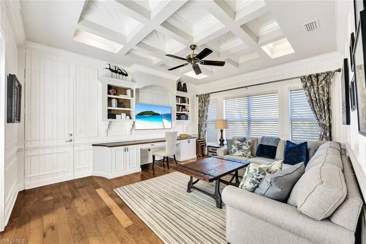 Den with designer furnishings, ceiling fan, coffered ceiling, hardwood floors, crown molding, built in desk and shelving