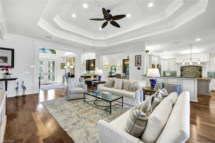 Living room featuring designer furnishings, built in shelves/cabinets, hardwood flooring, a tray ceiling, and crown molding