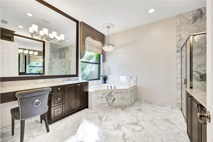 Primary bathroom featuring soaking tub, shower, double vanities, a healthy amount of sunlight, and an inviting chandelier