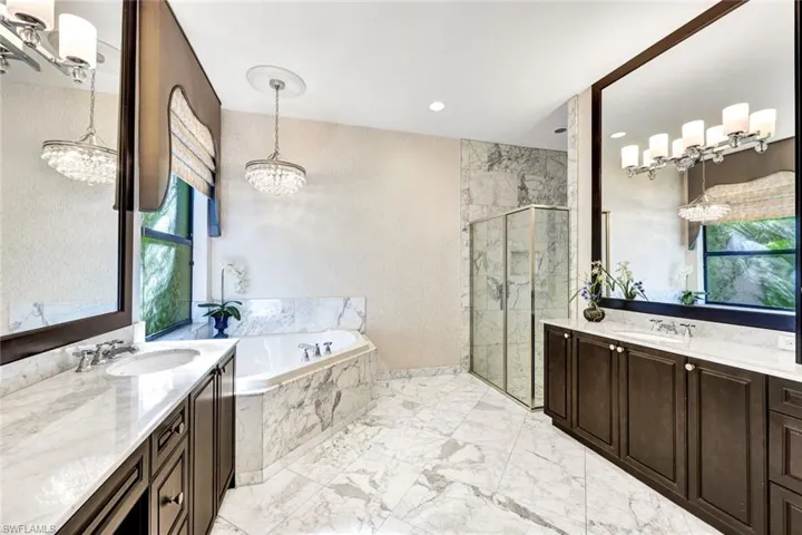 Primary bathroom featuring soaking tub, shower, double vanities, a healthy amount of sunlight, and an inviting chandelier