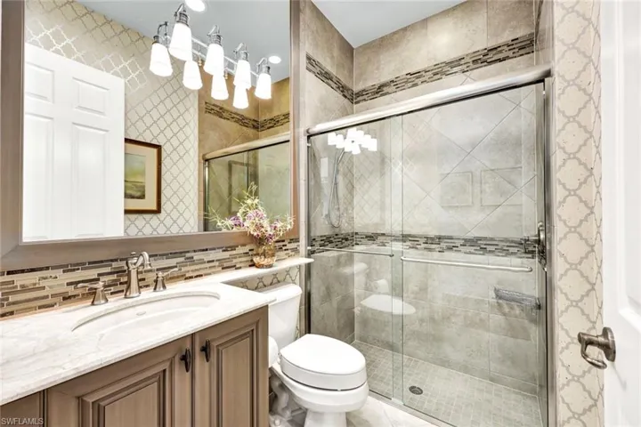 Main bathroom featuring vanity, tile patterned floors, decorative backsplash, toilet, and an enclosed shower