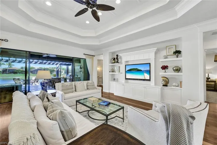 Living room featuring designer furnishings, built in shelves/cabinets, hardwood flooring, a tray ceiling, and crown molding