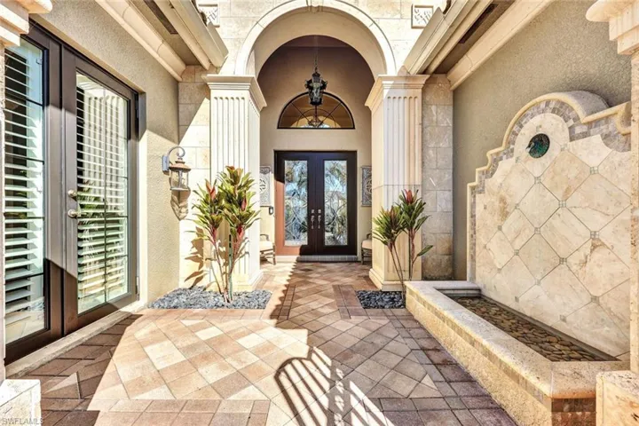 Gated courtyard featuring stone fountain, double glass entry doors and custom lighting