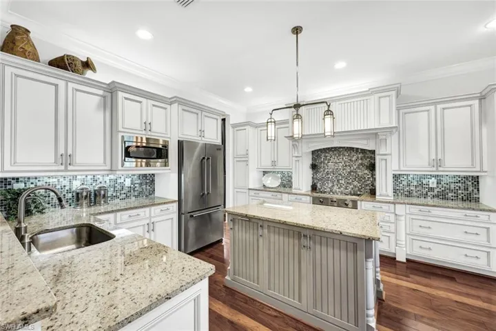 Kitchen with backsplash, hardwood floors, light stone countertops, custom window treatments, decorative light fixtures, and Viking appliances