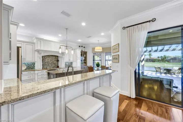Kitchen with backsplash, hardwood floors, light stone countertops, custom window treatments, decorative light fixtures, and Viking appliances