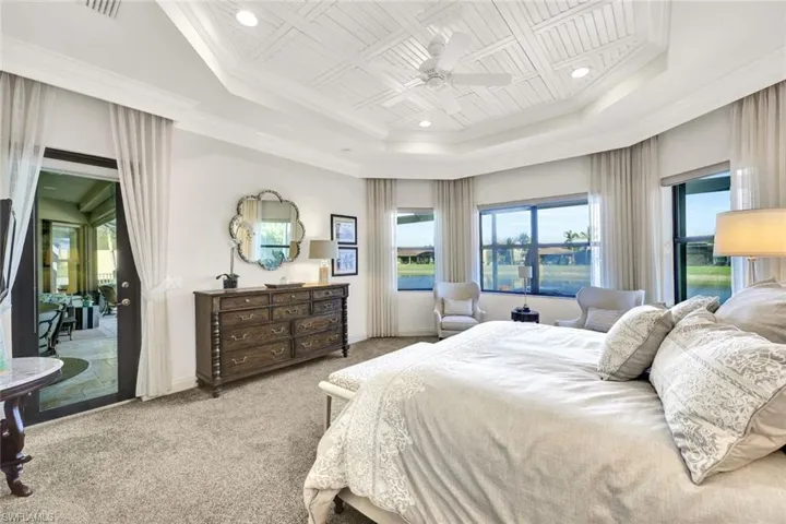 Primary bedroom with a tray ceiling, new carpet, custom window treatments, new carpet, access to exterior, ceiling fan, and extensive molding & trim