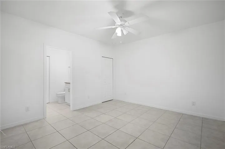 Unfurnished bedroom with light tile patterned flooring, ceiling fan, and ensuite bathroom