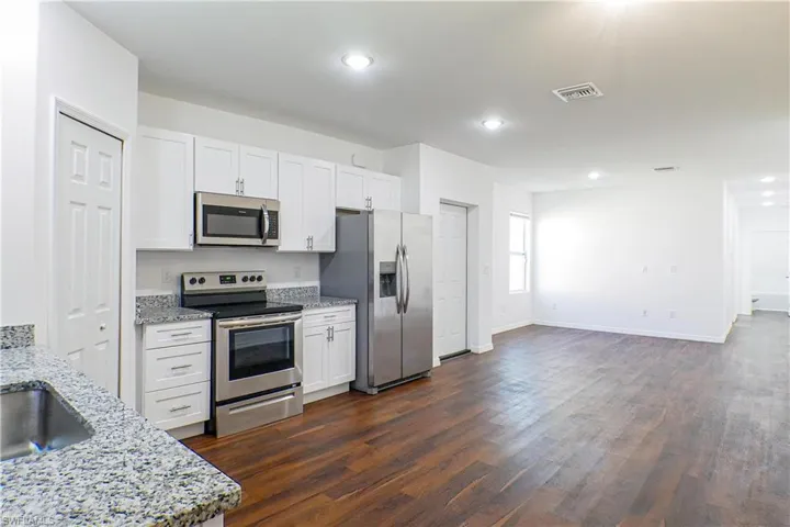 Kitchen with stainless steel appliances, light stone counters, dark wood-style flooring, white cabinetry, and recessed lighting