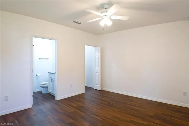 Unfurnished bedroom with dark wood-style floors, ceiling fan, and ensuite bathroom
