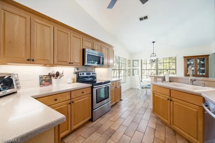 Kitchen with stainless steel appliances, light countertops, lofted ceiling, decorative light fixtures, and wood tiled floors