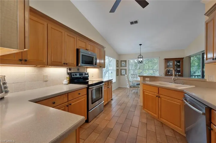 Kitchen featuring appliances with stainless steel finishes, vaulted ceiling, pendant lighting, wood tiled floors, and light countertops