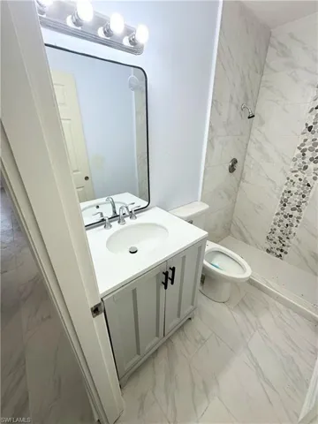 Bathroom with toilet, a tile shower, tile patterned flooring, and vanity