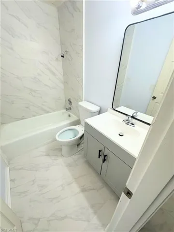 Full bathroom with tiled shower / bath combo, toilet, tile patterned floors, and vanity
