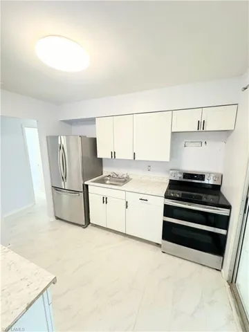 Kitchen featuring appliances with stainless steel finishes, white cabinetry, light tile patterned floors, and sink