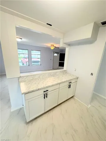 Kitchen featuring light stone counters, white cabinets, light tile patterned floors, kitchen peninsula, and ceiling fan