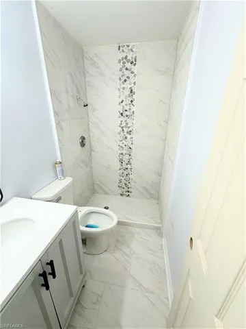 Bathroom featuring tile patterned floors, toilet, a tile shower, and vanity