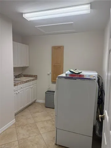 Washroom featuring baseboards, light tile patterned flooring, washer / dryer, cabinet space, and a sink