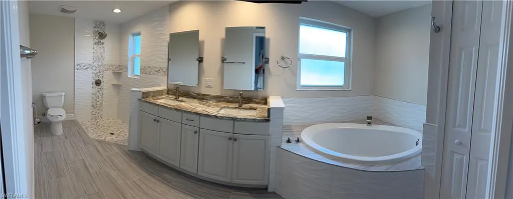Bathroom with a sink, walk in shower, double vanity, and a garden tub