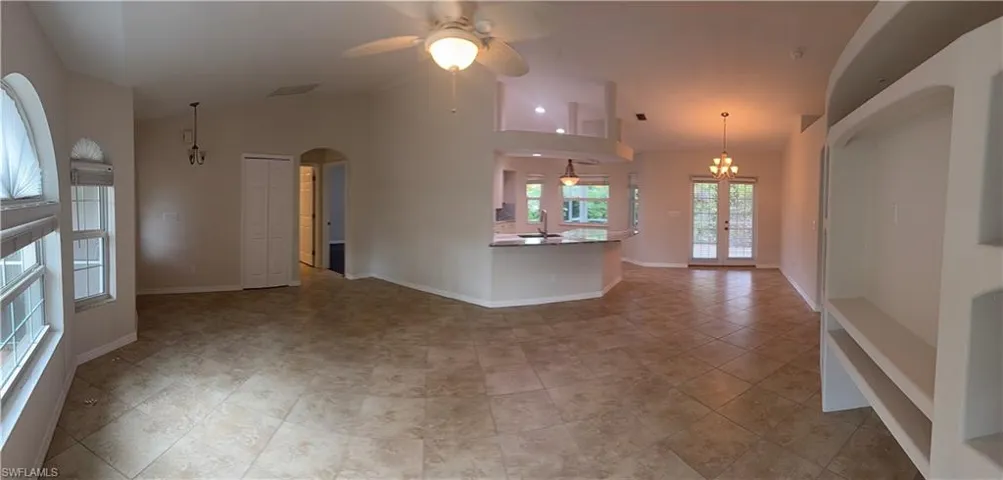 Unfurnished living room featuring arched walkways, ceiling fan with notable chandelier, a sink, and baseboards